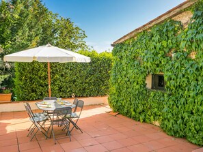 Une terrasse extérieure avec une table et des chaises, un parasol blanc et un mur recouvert de lierre.