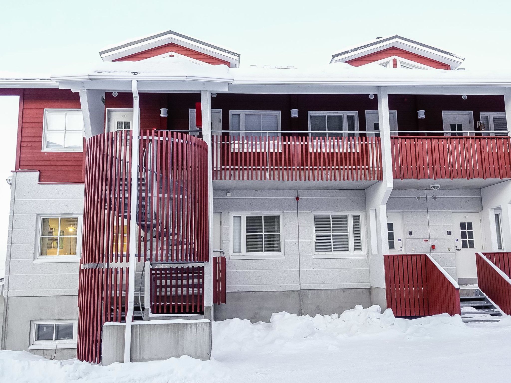 A multi-story building with a red and white facade, balconies, and a gated entrance.