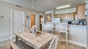 A modern kitchen with white cabinetry, a dining area with a wooden table and white chairs, and a ceiling fan. - *Sept 20 - 26th Open! 2 King Beds! Huge Balcony! (Panama City Beach)