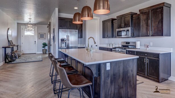 A modern kitchen with dark wood cabinets, a large island with bar stools, stainless steel appliances, and pendant lighting. - Parking galore, quiet & bonus- electrical RV hookup! (Saint George)