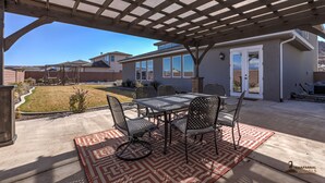 An outdoor patio with a pergola, a table with chairs, and a patterned rug. - Parking galore, quiet & bonus- electrical RV hookup! (Saint George)
