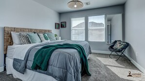 A bedroom with a bed, a hanging light fixture, and a window with blinds.