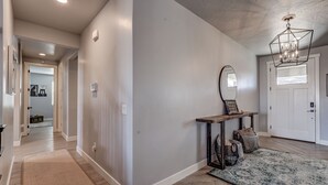 A hallway with a wooden floor, a rug, a bench with a mirror, and a chandelier.