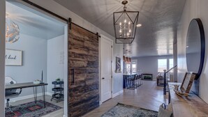 A spacious interior with a wooden sliding door, a dining area with striped chairs, and a kitchen in the background. - Parking galore, quiet & bonus- electrical RV hookup! (Saint George)