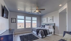 Une chambre à coucher avec un lit, un ventilateur de plafond, une télévision et de grandes fenêtres donnant sur les montagnes.