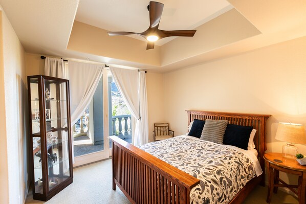 A bedroom with a bed, a nightstand, a lamp, a ceiling fan, and a glass cabinet.
