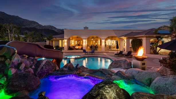 A pool area with a hot tub, lounge chairs, and a building with arched windows in the background. - Hidden Oasis: Pickleball Basketball Waterslide Game Room Gym! ⭐️⭐️⭐️⭐️⭐️ (Palm Desert)