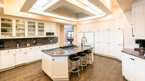 A modern kitchen with white cabinetry, a central island with stools, and a skylight above. - Hidden Oasis: Pickleball Basketball Waterslide Game Room Gym! ⭐️⭐️⭐️⭐️⭐️ (Palm Desert)