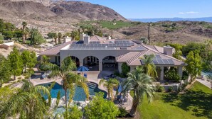 A large house with a swimming pool, solar panels, and a mountainous backdrop. - Hidden Oasis: Pickleball Basketball Waterslide Game Room Gym! ⭐️⭐️⭐️⭐️⭐️ (Palm Desert)
