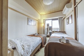 Une chambre d’hôtel avec deux lits, une grande fenêtre avec des rideaux, un ventilateur de plafond et un climatiseur fixé au mur.