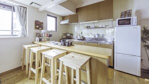 A kitchen with wooden cabinets, a white refrigerator, a microwave, and a bar area with stools. - Nestle Tokyo Deluxe Akihabara 02 (Tokyo)