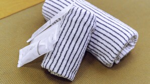 A neatly folded striped towel and a white plastic bag on a textured surface. - Nestle Tokyo Deluxe Akihabara 02 (Tokyo)