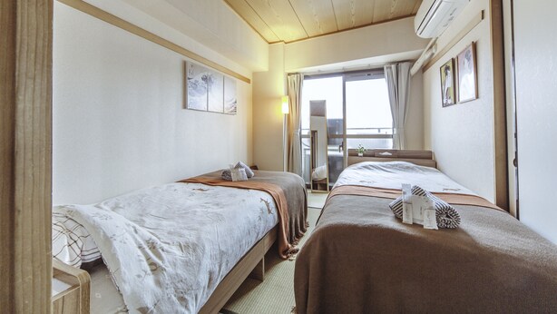 A hotel room with two beds, a large window with curtains, a ceiling fan, and a wall-mounted air conditioner. - Nestle Tokyo Deluxe Akihabara 02 (Tokyo)