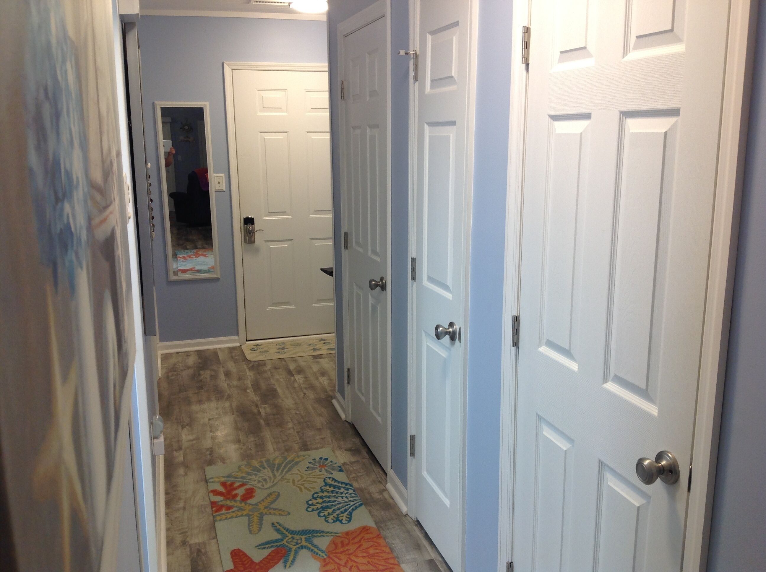 A hallway with two white doors, a wooden floor, and a colorful rug.