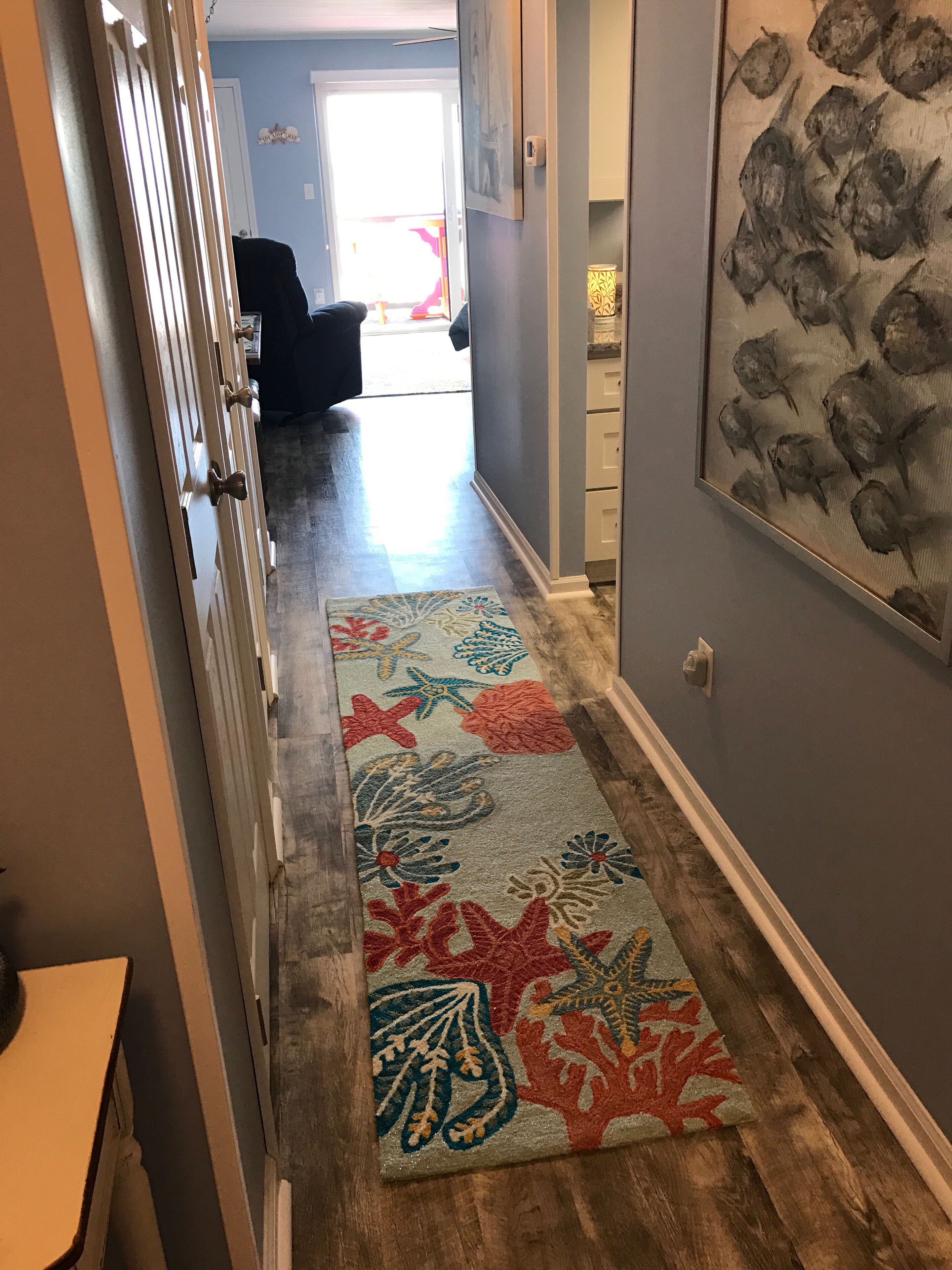 Ein Korridor mit einem gemusterten Teppich, einem Fischgemälde in einem Rahmen und einer Tür zu einem Zimmer.