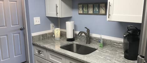 A kitchen with white cabinets, a granite countertop, a stainless steel sink, a coffee maker, and a decorative sign above the cabinets.