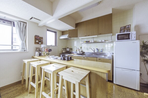 A kitchen with wooden cabinets, a white refrigerator, a microwave, and a bar area with stools.