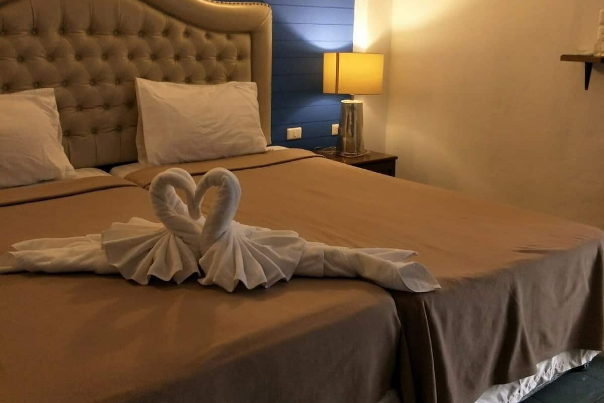 A hotel room with a large bed, a headboard, a bedside lamp, and a wall-mounted shelf.