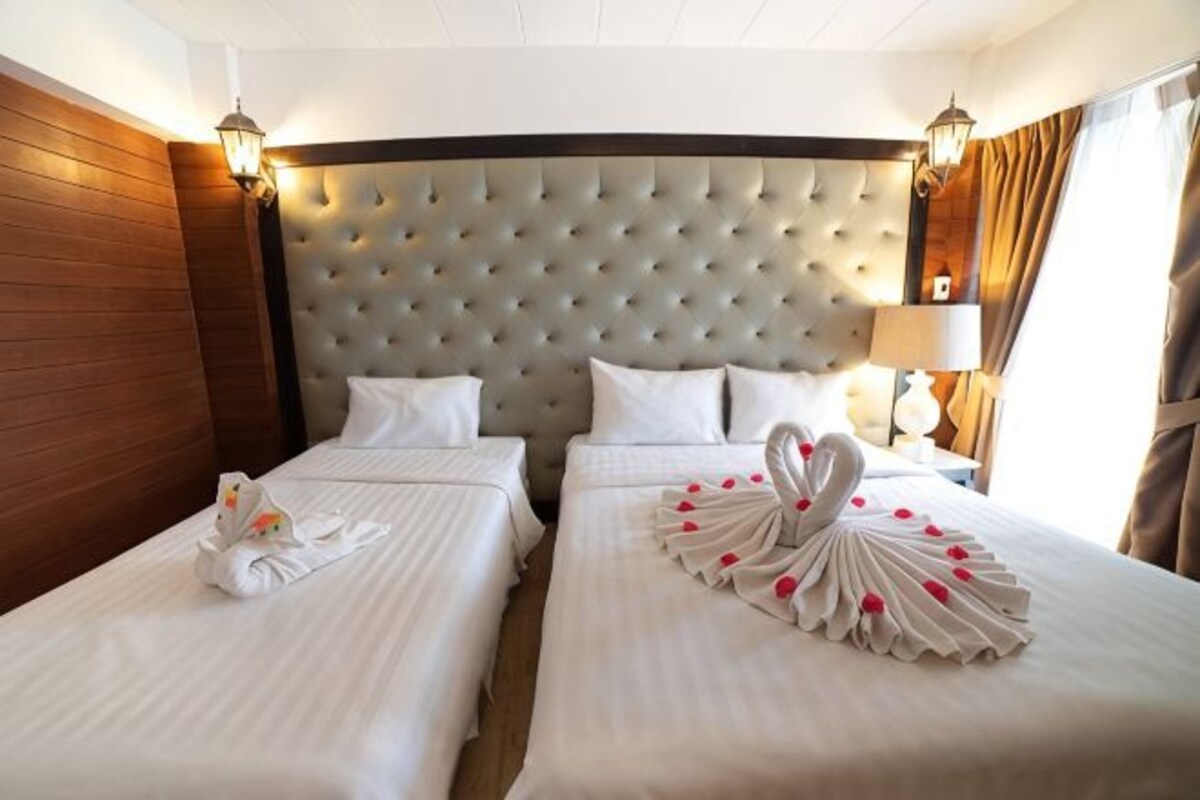 A hotel room with two beds, a tufted headboard, bedside lamps, and a decorative swan on the beds.