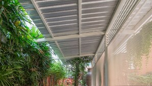 A covered outdoor seating area with white metal chairs and tables, surrounded by lush greenery and a corrugated metal roof. - At 42 Residence (Bangkok)