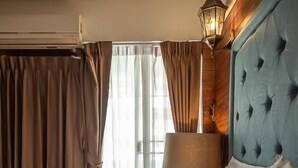 A hotel room with a large bed, a wooden headboard, a window with curtains, and a lamp on the nightstand. - At 42 Residence (Bangkok)