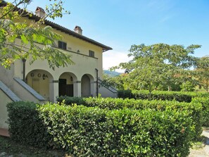Traditional Mediterranean-style building with a symmetrical entrance and covered staircase, set amidst lush gardens.