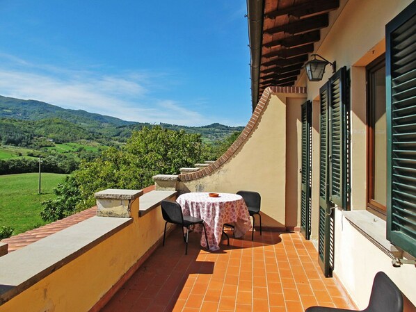 A balcony with a table and chairs, overlooking a green landscape with hills.