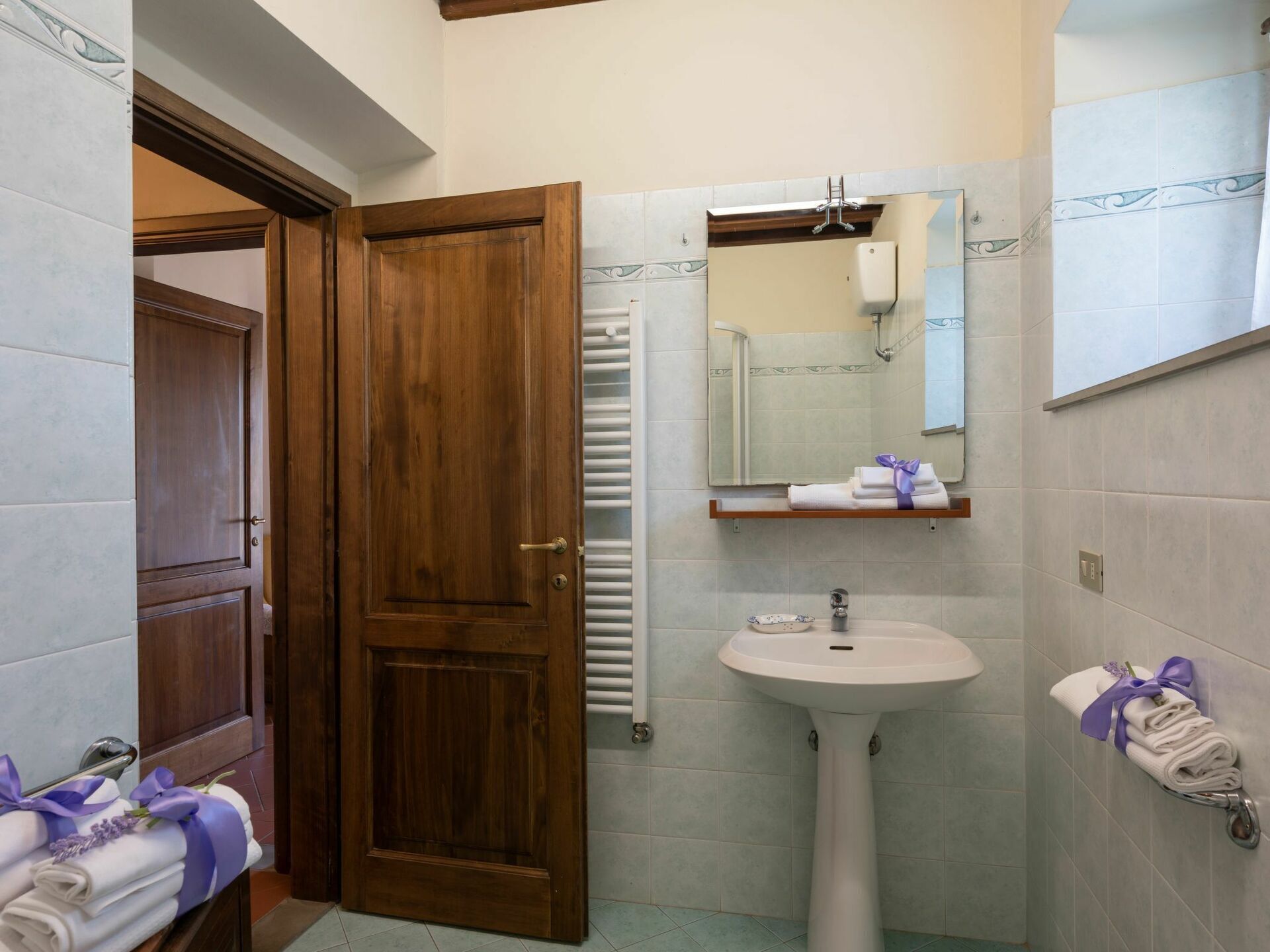 Un bagno con una porta in legno, un lavabo su piedistallo, uno specchio e asciugamani su uno scaffale.