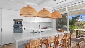 Cocina moderna con armarios blancos, una isla grande con taburetes de bar y tres lámparas colgantes tejidas.