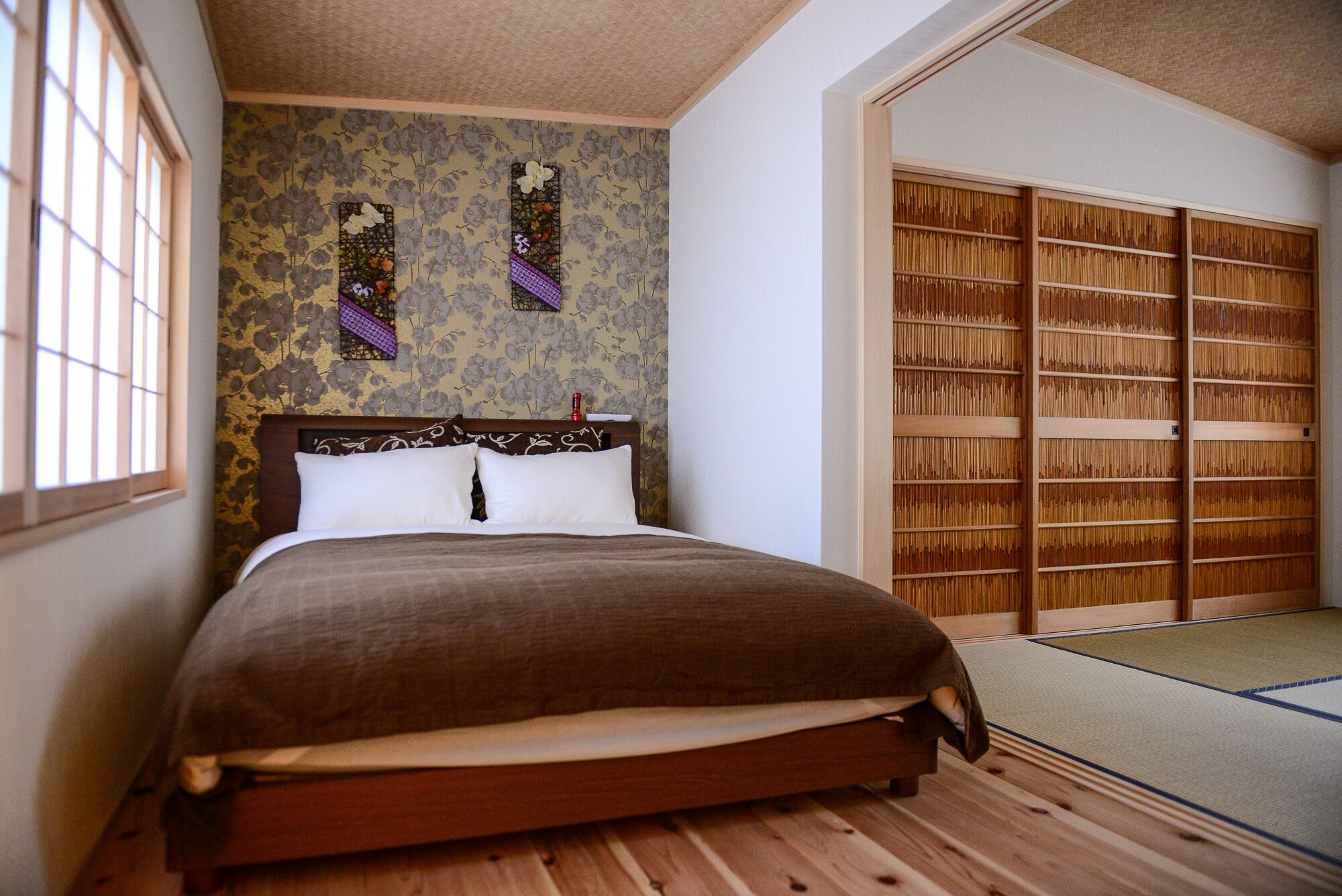 A traditional Japanese-style bedroom with a tatami mat floor, a wooden bed with a headboard, and a shoji screen with floral patterns.