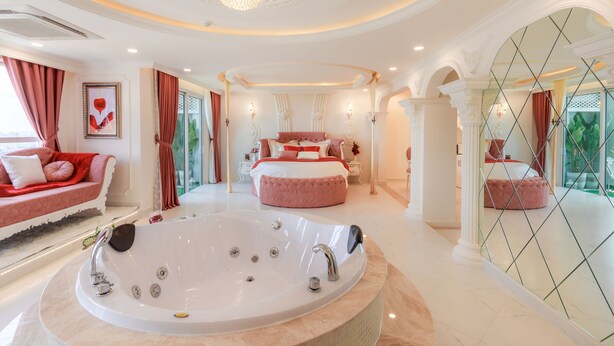 A luxurious bedroom with a large bathtub, a plush sofa, and a classic chandelier.