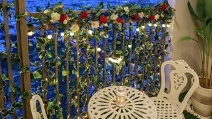 A balcony with a view of a cityscape, decorated with flowers and string lights.