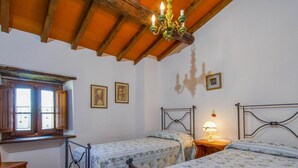 A bedroom with two beds, wooden ceiling beams, a window with shutters, and a chandelier. - Lovely apartment in villa for 4 people with pool, WIFI (Loro Ciuffenna)