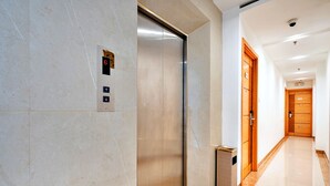 An elevator with a digital display, a trash bin, and a wooden door in a hallway with a tiled floor. - S79 Son Mi Hotel 839 Le Hong Phong Street (Ho Chi Minh City)
