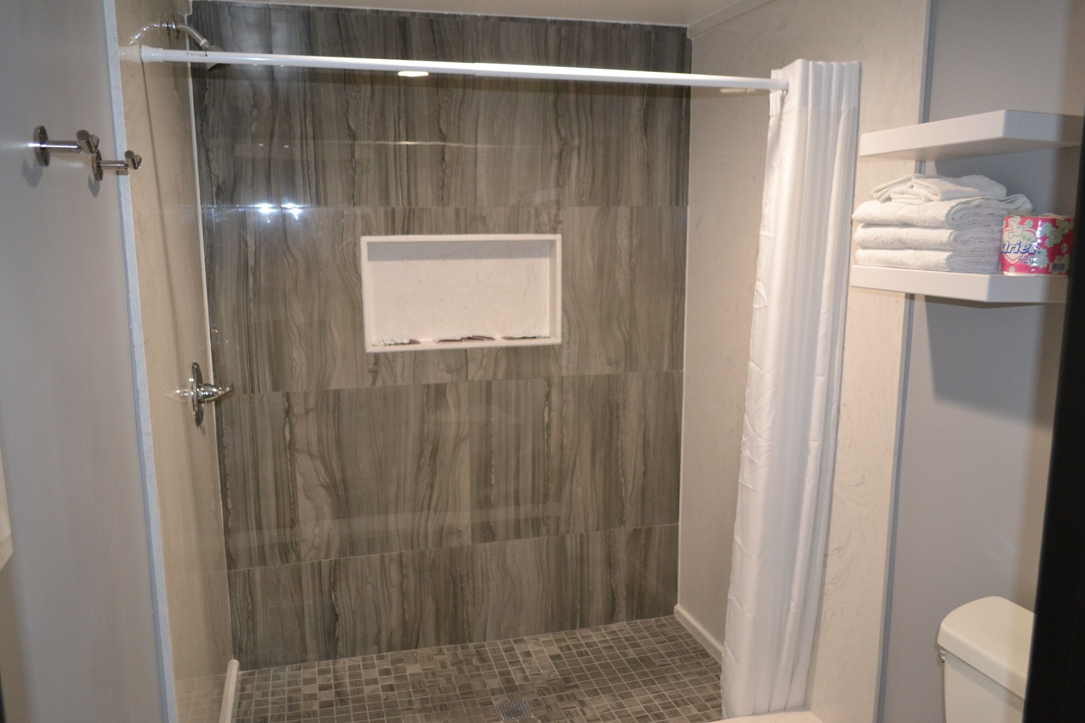 A shower with a glass door, a tiled floor, and a white towel rack with folded towels.