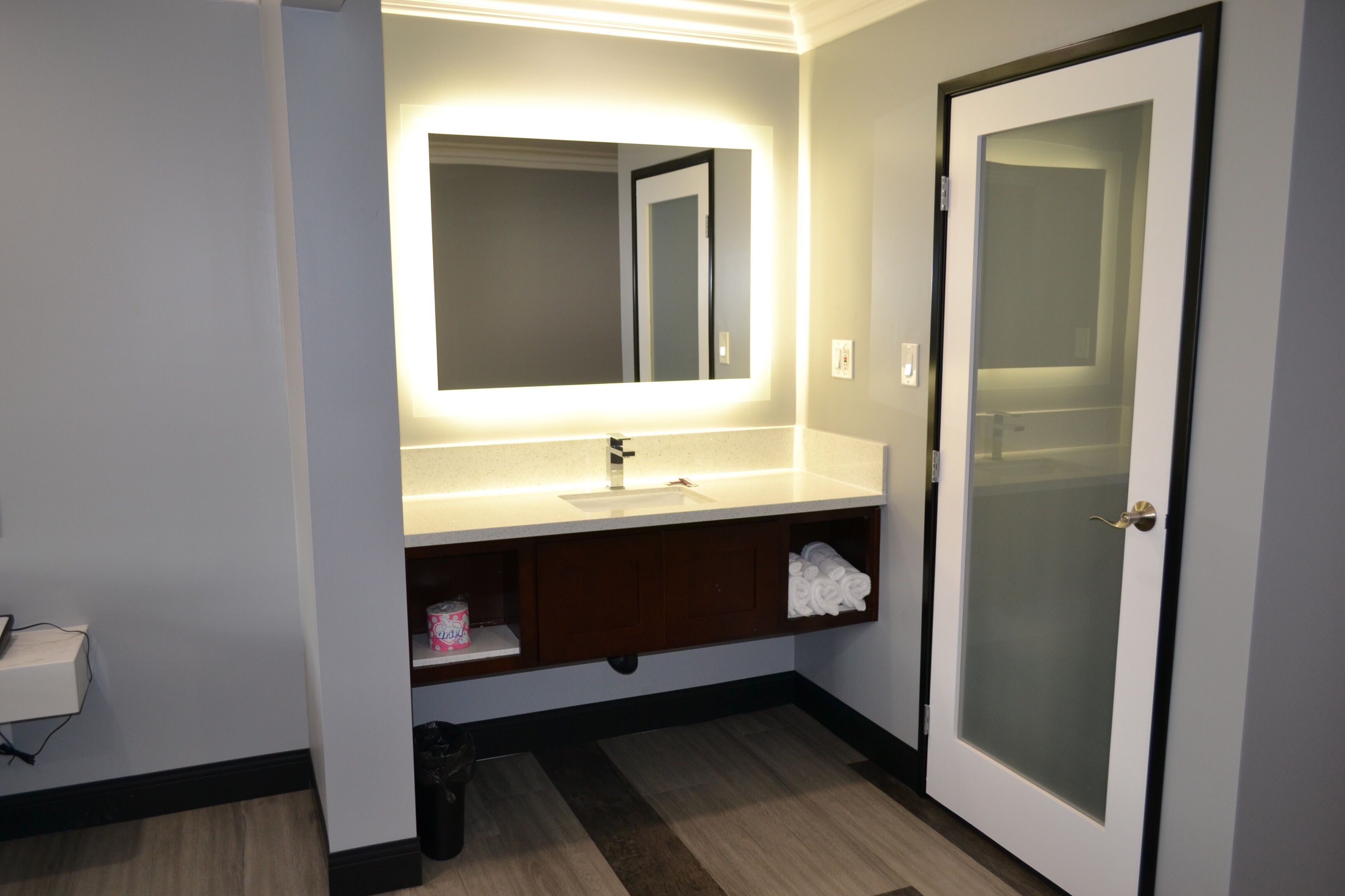 Un baño moderno con un espejo grande, lavamanos blanco y puerta de vidrio.