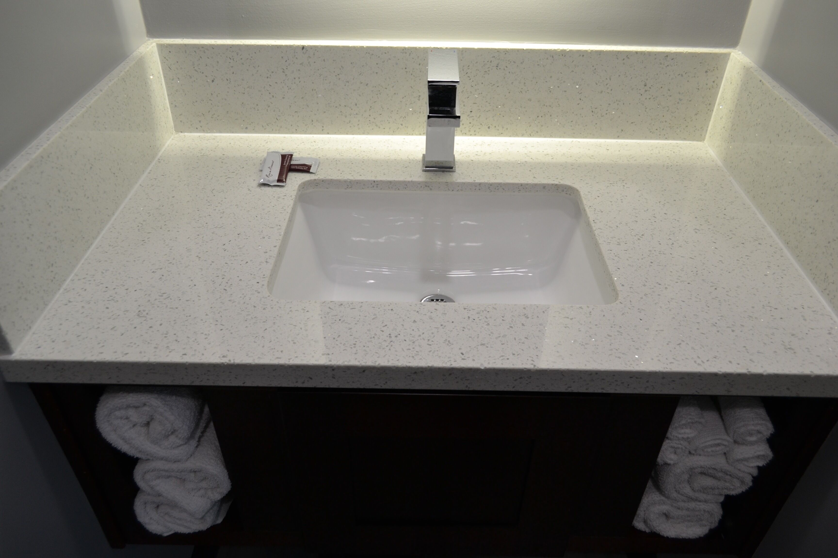 A bathroom with a white speckled sink, a modern faucet, and a towel rack with folded towels.