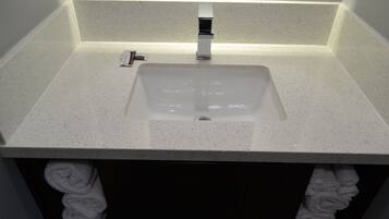 A bathroom with a white speckled sink, a modern faucet, and a towel rack with folded towels.