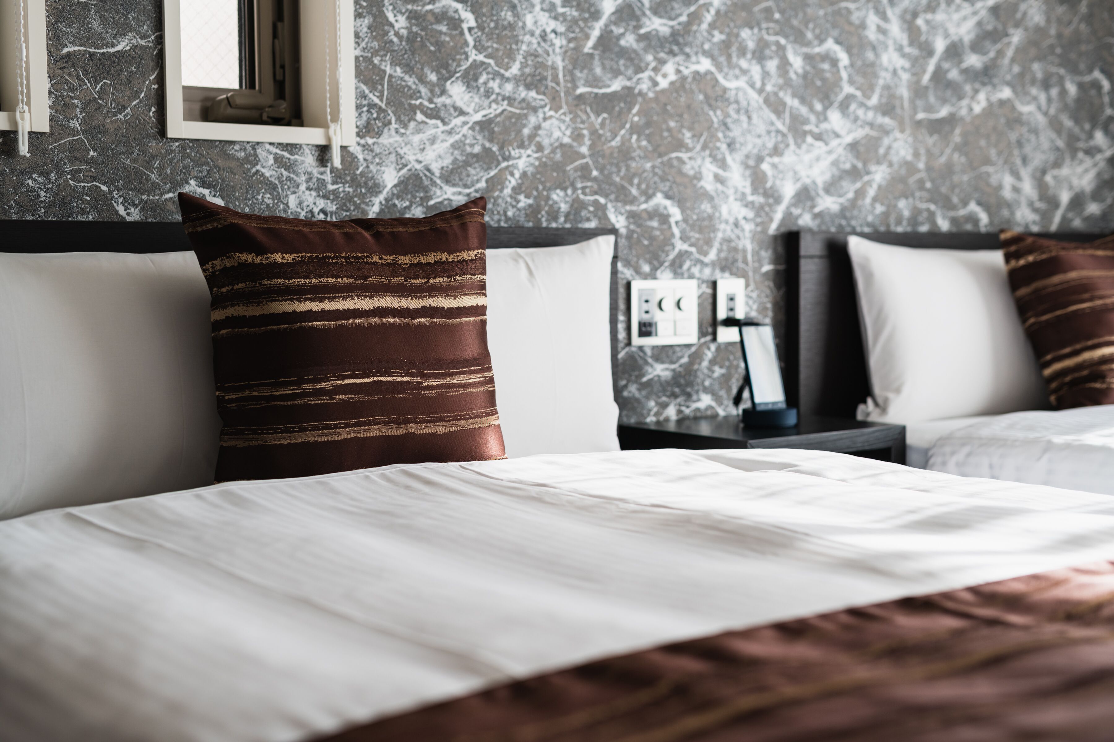 A hotel room with a marble-patterned wall, a bed with white bedding, and two nightstands with lamps.