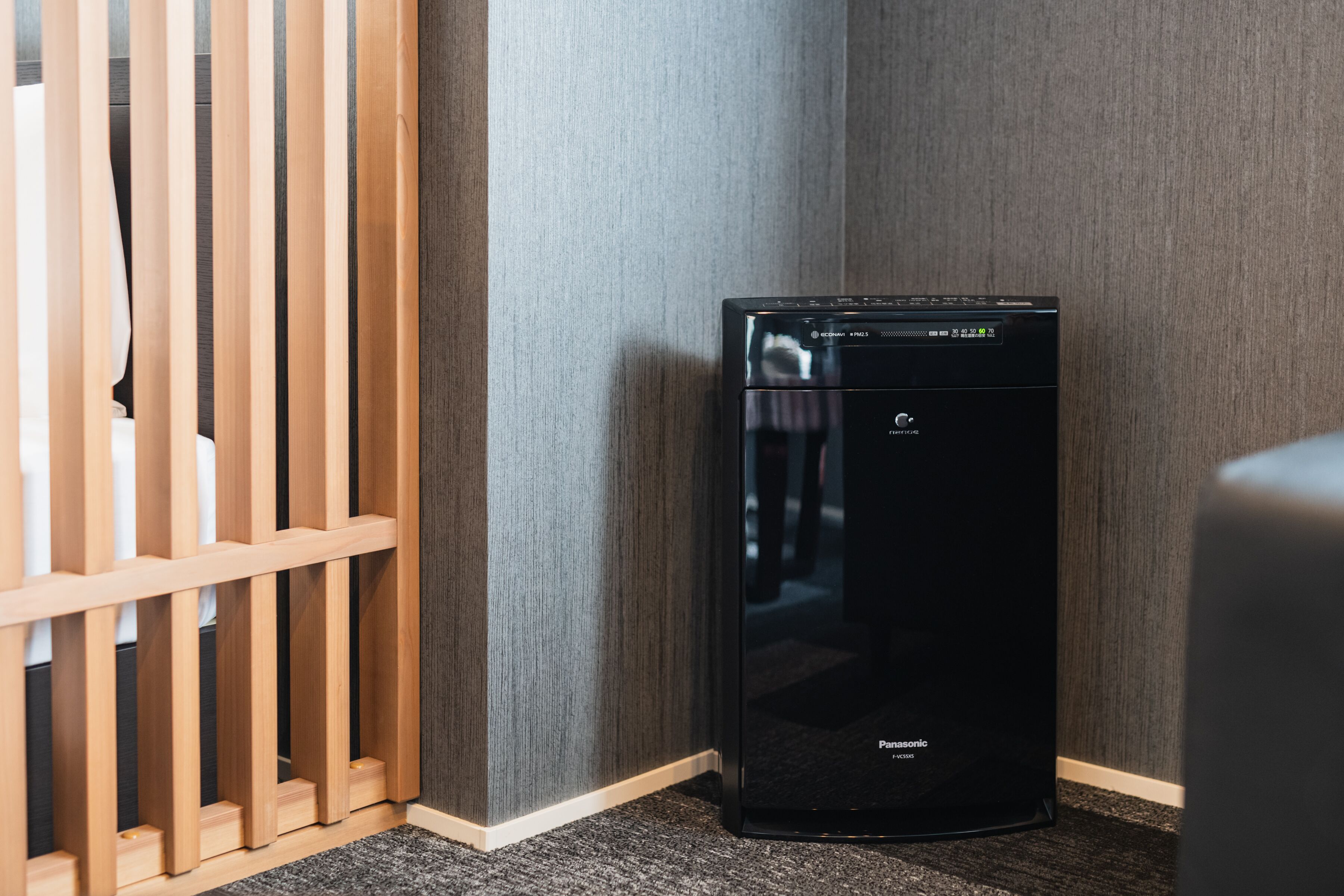A black Panasonic dishwasher in a corner of a room with a wooden partition and a grey wall.