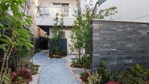 Um edifício residencial moderno com um caminho estreito que leva à entrada, rodeado por diversas plantas e um muro de pedra.