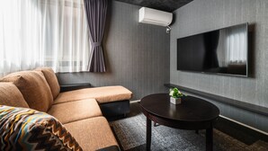 Quarto de hotel moderno com sofá, uma pequena mesa, televisão de tela plana na parede e aparelho de ar condicionado.