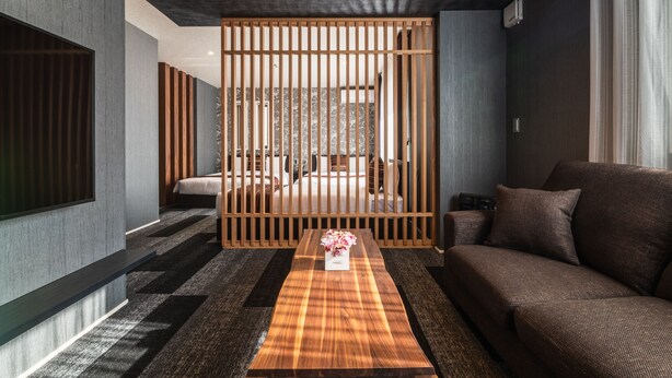 Uma sala de estar moderna com um sofá, uma mesa de centro de madeira com um arranjo floral e um painel deslizante.