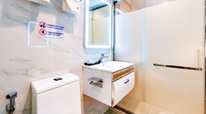 Een moderne badkamer met een marmeren wand, een wastafel met spiegel, een toilet en een douchegedeelte.