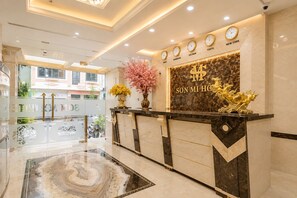 Een hotel receptiebalie met een marmeren vloer, een klok die meerdere tijdzones weergeeft, en een decoratieve gouden beeldhouwkunst van een paard.