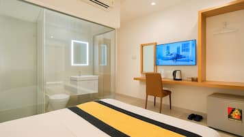 Quarto de hotel com cama, escrivaninha, cadeira, televisão, espelho, guarda-roupa e pequeno armário.