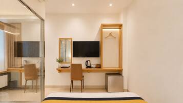 Ein modernes Hotelzimmer mit Bett, Schreibtisch mit Fernseher, Stuhl und einer kleinen Küchenzeile.