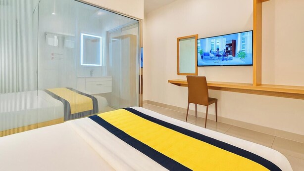 Hotelkamer met een bed, bureau, stoel, televisie en een glazen scheidingswand.