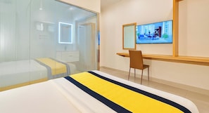 Camera d'albergo con un letto, una scrivania, una sedia, un televisore e un divisorio in vetro.