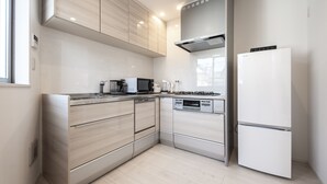 A modern kitchen with light wood cabinets, stainless steel appliances, and a white refrigerator. - Private Hotel Oshiage (Tokyo)